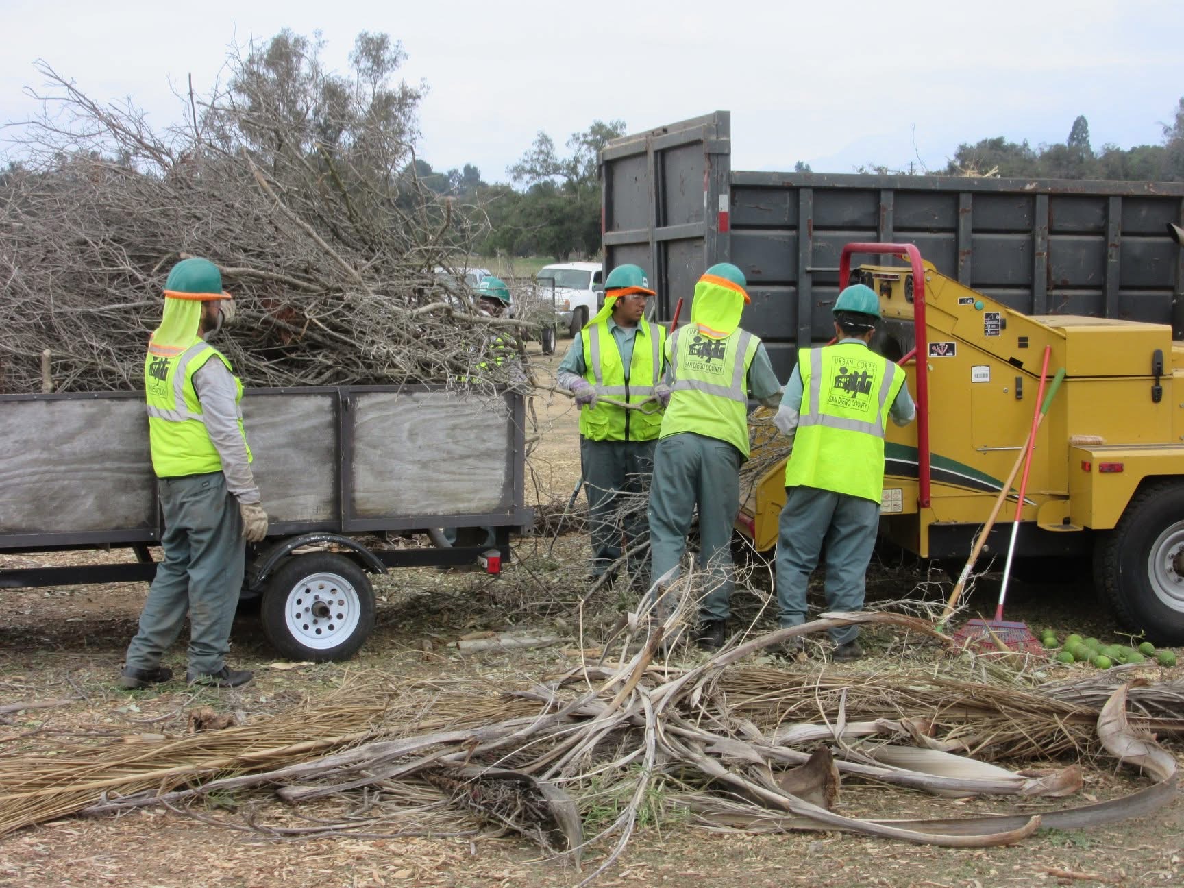 Volunteers in high-visibility vests loading cleared brush into a trailer during a community cleanup.