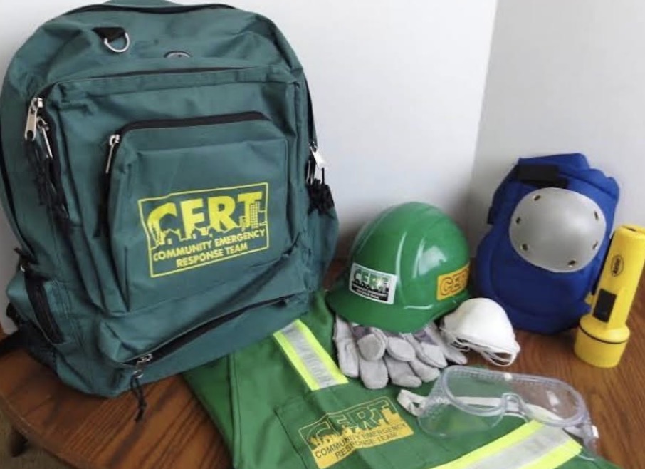 Green CERT Community Emergency Response Team backpack with hard hat, reflective safety vest, gloves, goggles, knee pads, and flashlight.
